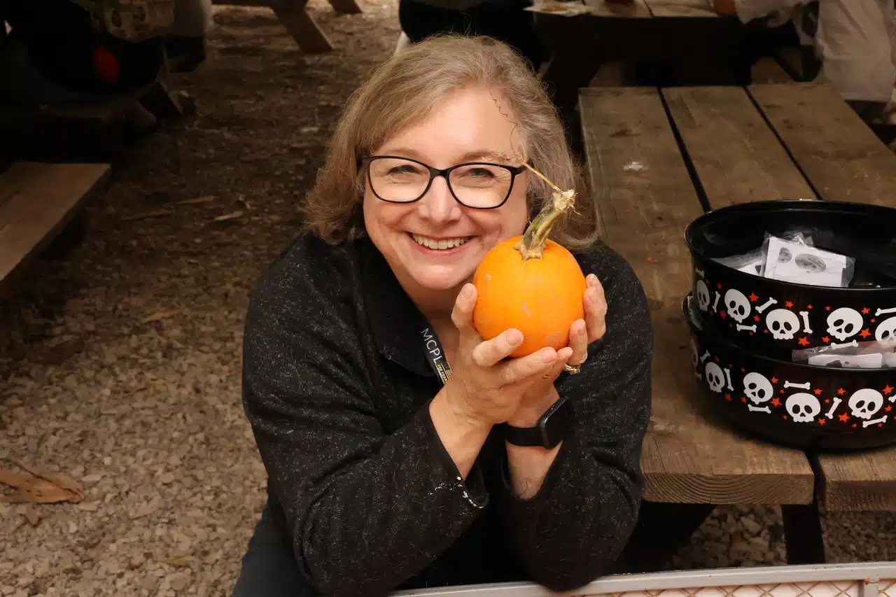 A librarian holds up a small pumpkin and smiles.