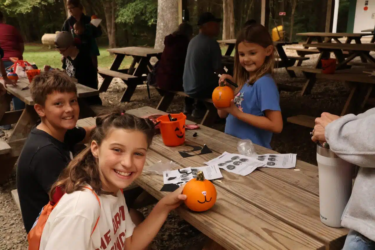 A group of kids smiling around a table with pumpkins. 