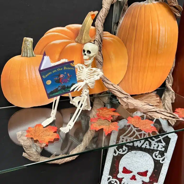 A toy skeleton reads a book with pumpkins in the background